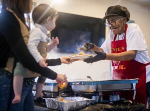 A woman in a red apron, white shirt and cap serves food to a woman and her infant at the North Charleston Garlic Crab Championship.