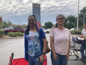 Wearing a blue and white patterned top and long brown braids, Carol Smith-Hill stands with her family member in line at Ingles grocery store. 