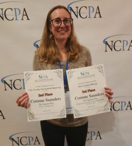 Saunders stands in front of an NCPA banner holding up two paper awards for her reporting.